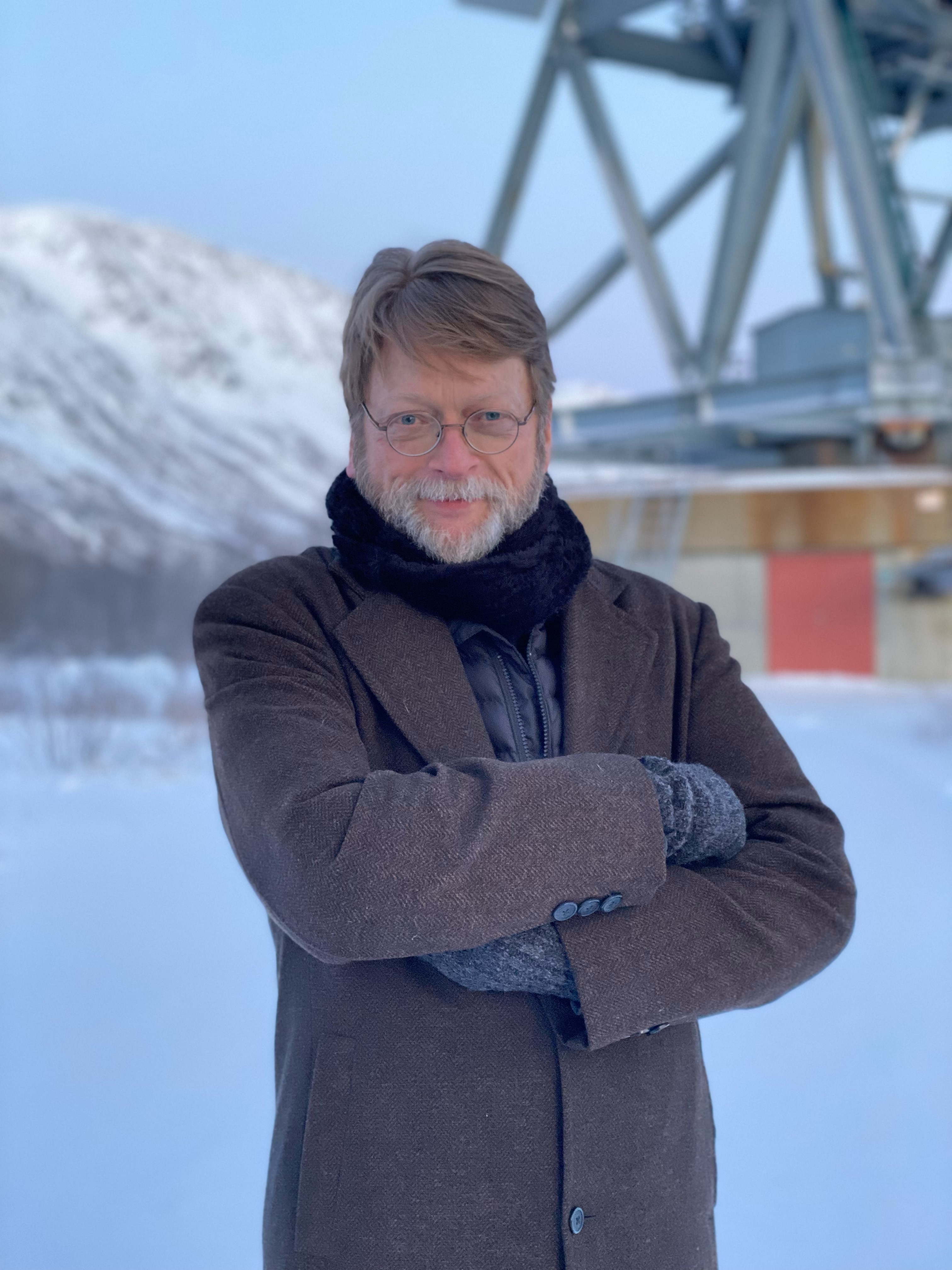 Douglas Vakoch standing in a snowy landscape near a radio telescope structure.